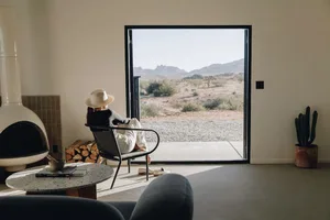 A minimalist living room with a modern terrazzo floor and floor-to-ceiling windows overlooking a desert landscape.