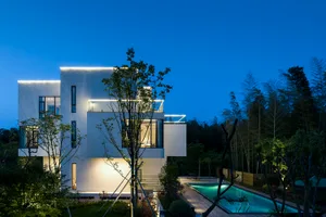A modern residential building with a white exterior and concrete walls, illuminated at night with warm lights.