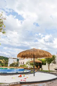 Residential swimming pool surrounded by sand with beach toys and a thatched umbrella.