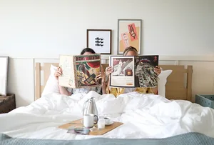 Two individuals laying in bed with open magazines in front of them.