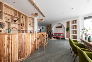 A cozy lounge area with wooden decor, including a guitar, books, and green chairs, creating a relaxing atmosphere.