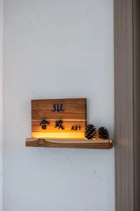 A wooden decorative shelf on a white wall with illuminated text and pinecones.