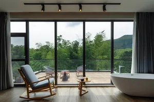A minimalist interior with an outdoor seating area on a wooden deck overlooking lush greenery.