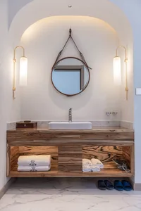 A modern bathroom features a wooden vanity with a marble countertop and a round mirror hanging above it.