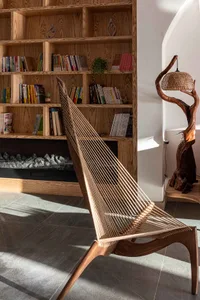 Modern, minimalist lounge area with wooden furniture, a bookshelf, a unique floor lamp, and a cozy atmosphere.