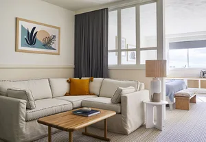 A modern living room with a white sectional sofa, wooden coffee table, and large windows.