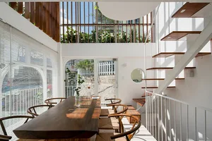 A modern indoor living space featuring a wooden dining table, glass walls, and a concrete staircase.
