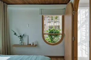 Minimalist bedroom with a bed, window, and plants, featuring wood, glass, and concrete materials.