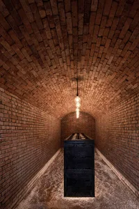 Industrial brick corridor with wooden box, illuminated by hanging light bulbs.