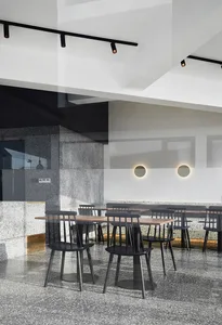 Industrial-style restaurant interior with concrete and terrazzo flooring, black chairs, and minimalist design.