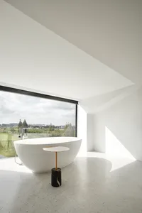 A minimalist bathroom with a freestanding white bathtub, a black and white marble table, and a large window with a view of th