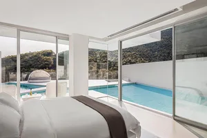 A minimalist bedroom featuring white walls, a glass wall, and a concrete floor.