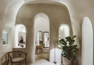 A minimalist interior space featuring polished concrete walls and archways, with a comfortable seating area and a potted plan