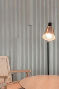 A minimalist interior space featuring wood and concrete materials with a floor lamp and round wooden table.
