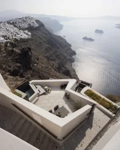 An outdoor seating area designed with a minimalist aesthetic, featuring concrete furniture and a view of the sea.
