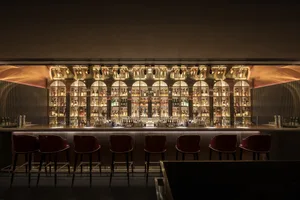 A modern bar with metal-clad shelves filled with bottles of alcohol and seating for patrons.