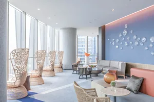 A contemporary hotel lobby featuring modern furniture, blue and white decor, and large windows with city views.