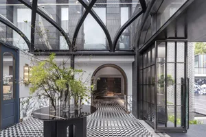 Modern hotel lobby featuring a glass rooftop window, concrete walls, and a patterned black and white floor.
