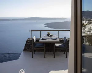 Modern minimalist balcony featuring glass railings and stone bench overlooking a serene ocean view.