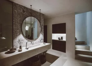 A minimalist bathroom with a concrete sink and wall, featuring a circular mirror and hanging lights.