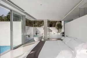 Modern minimalist bedroom with glass walls and white surfaces.