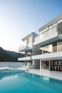Modern residential house with glass walls, concrete balconies, and a swimming pool overlooking mountains.
