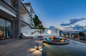 Modern residential patio with a concrete seating area, a pool, and a tree, set against a twilight sky with clouds.