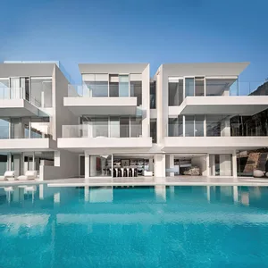 A modern residential pool house featuring white stone and glass exterior materials.
