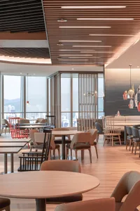 A modern, minimalist restaurant interior with wooden tables and chairs, large windows offering a view of the city, and a warm