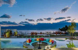 A circular seating area with colorful cushions overlooking a serene lake and mountains at dusk.