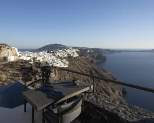 A wooden table and chairs overlooking the ocean and a coastal town on a cliffside.