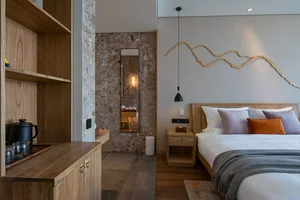 Modern minimalist bedroom featuring a bed with white bedding and orange pillows, a wooden headboard, and a side table with a