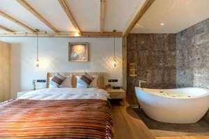 Modern minimalist bedroom with wood and marble materials, featuring a large bed with colorful textiles and a freestanding bat