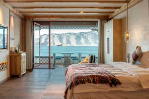 Modern hotel suite with wooden floor, ceiling, and furniture, featuring a balcony overlooking a lake and mountainous landscap