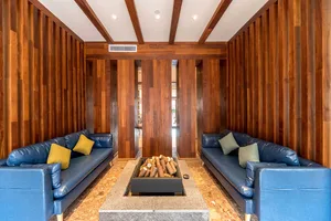 A modern interior living room with wooden walls and blue sofas arranged around a fire pit.