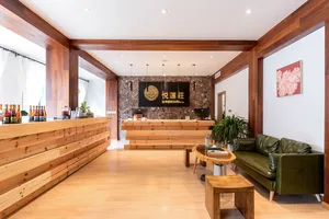 Modern lobby interior with wooden furniture and decor, featuring a green leather sofa, wooden tables, and a reception desk.