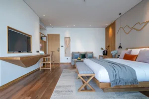 A modern minimalist bedroom featuring a wooden bed and furniture, with a flat-screen TV mounted on the wall and a grey and wh