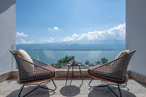 Two modern patio chairs with cushions and a small table with tea set, overlooking a vast ocean under a clear blue sky with sc