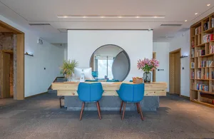 A modern reception desk made of wood, featuring blue chairs and a circular mirror.