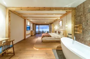 A modern residential bedroom suite with wooden floors, a bathtub, a cozy seating area, and a view of the mountains.