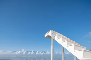 A modern staircase with white painted wooden steps and railings leading down to a beach or waterfront.