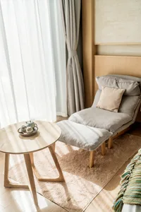A minimalistic relaxation area featuring a fabric-covered chair, a wooden table, and glass elements.