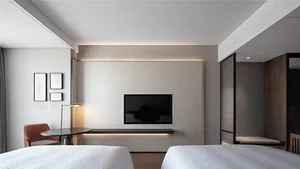 A minimalist bedroom with a modern aesthetic, featuring white beds, a TV mounted on the wall, and a floor lamp.