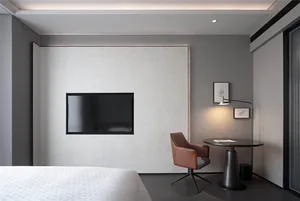 A minimalist bedroom featuring a black leather chair, a flat-screen television mounted on the wall, and a small round table w