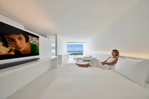 A woman lounging on a minimalist bed in a modern suite with a view of the sea.