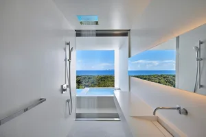 Modern minimalist bathroom with glass shower walls overlooking a scenic ocean view.