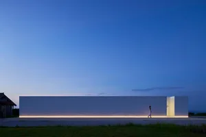 Modern exterior building with a white facade and concrete construction, illuminated by ambient lighting against a twilight sk