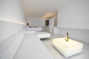 A minimalist living room with white furniture and concrete walls and floor