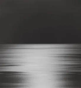 A black and white photograph of a blurred ocean scene at night