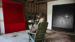 A minimalist artist's studio featuring a red and black canvas hanging on the walls, with a man sitting on a green chair in th